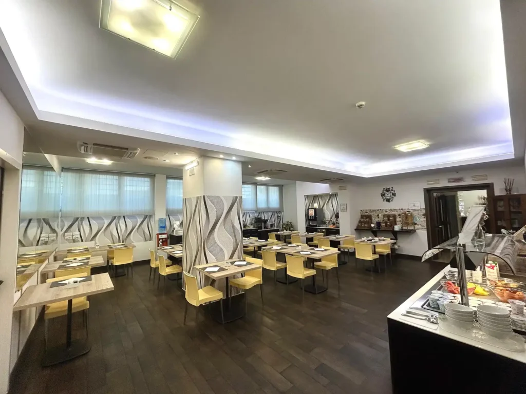 In the picture, a view of the breakfast room of the Cesena Hotel: we can see some tables and, on the right, a glimpse of the breakfast buffet.